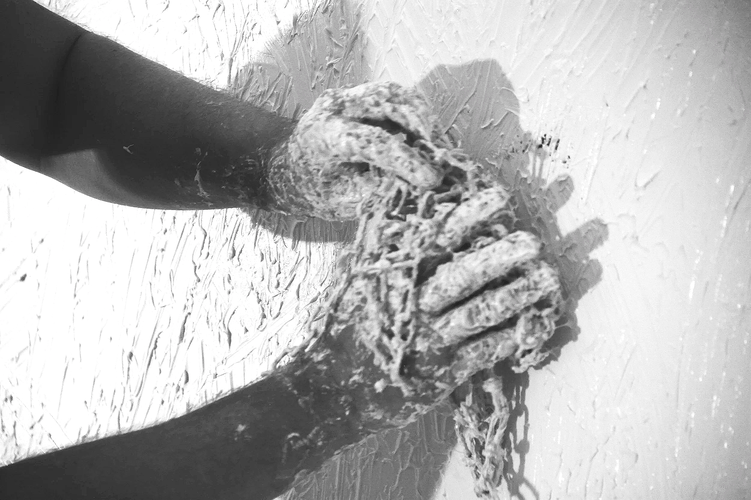 A black-and-white detail photograph showing abstract artist Christopher Durst working directly on the surface of a large-scale painting. Using his hands to manipulate thick acrylic medium and texture, the image captures the physical mark-making, expe